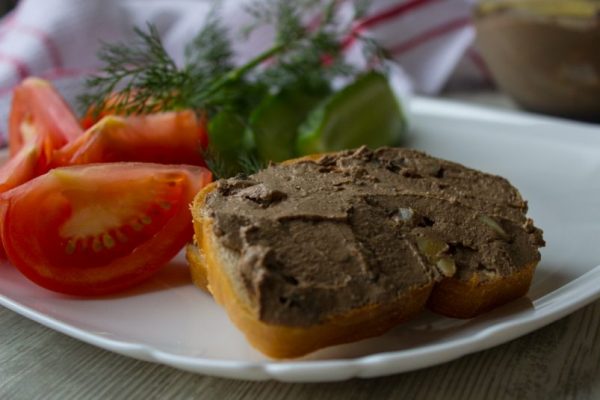 Хлеб с паштетом из куриной печени, свежие овощи и зелень на тарелке