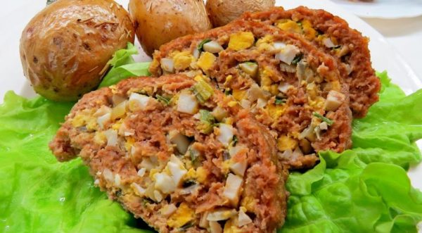 Нарезанный порционными кусочками мясной рулет с яично-луковой начинкой на тарелке с гарниром из картофеля и листьев салата