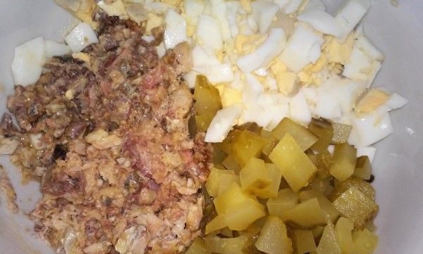 Нарезанные кубиками солёные огурцы и яйца в миске с измельчённой консервированной рыбой