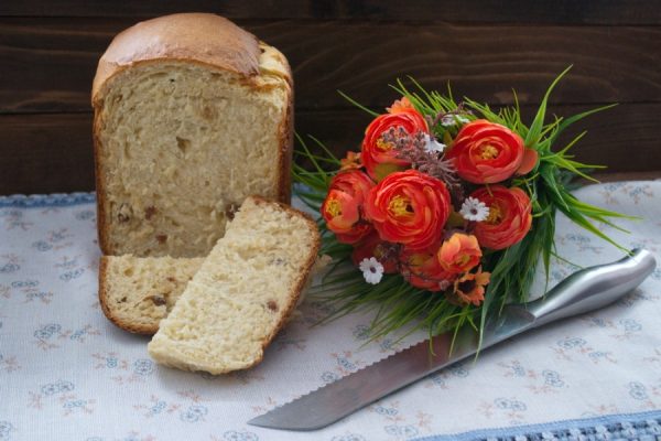 Творожный кулич на столе с букетом цветов и металлическим ножом