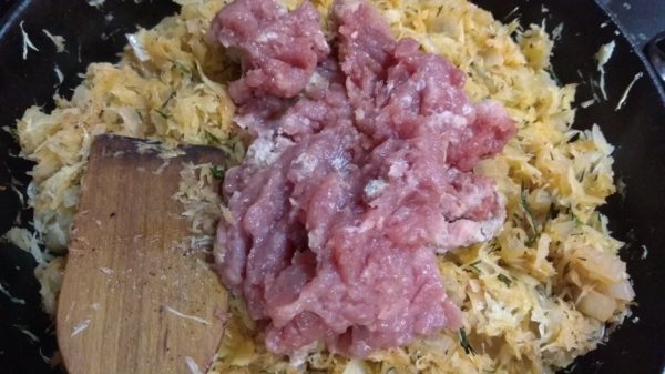 Сырой мясной фарш в сковороде с тушёной капустой