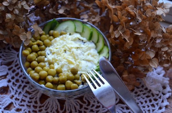 Салат с курицей, черносливом и консервированным горошком в маленьком салатнике с металлическими столовыми приборами