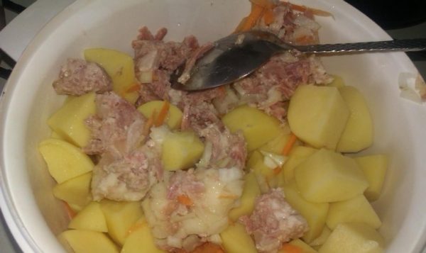 Нарезанный кубиками сырой картофель с кусочками тушёнки, рубленым репчатым луком и тёртой морковью в белой ёмкости